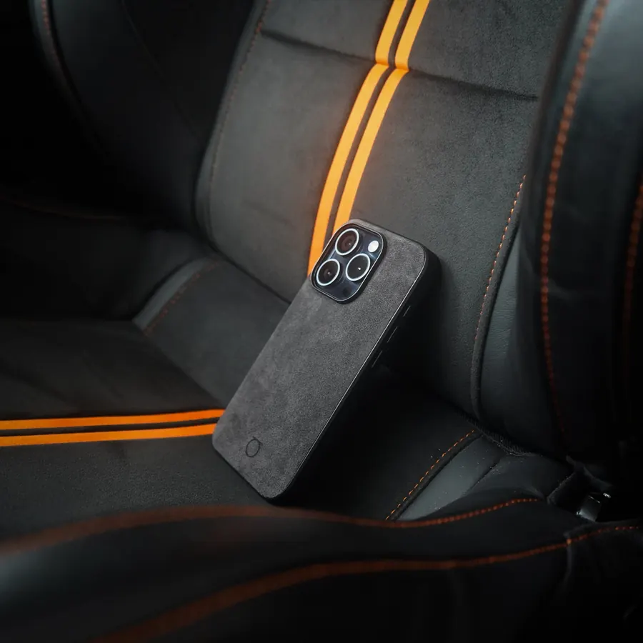A Graphite Alca Club case resting on an Alcantara sports seat with orange racing stripes